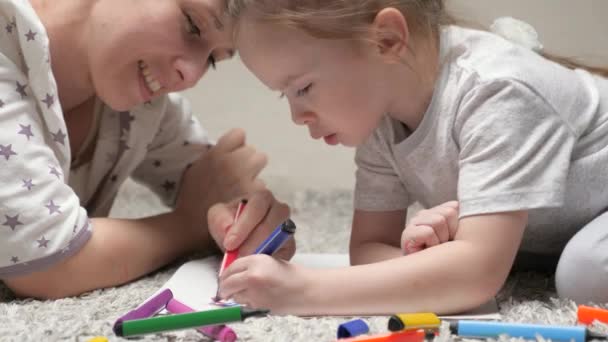 Barn och mamma, barnflicka, lär flickan att rita. Glad familj som leker hemma på golvet. En mamma hjälper sin dotter lära sig att rita på papper, färgläggning med flerfärgade pennor och filtspets pennor. — Stockvideo