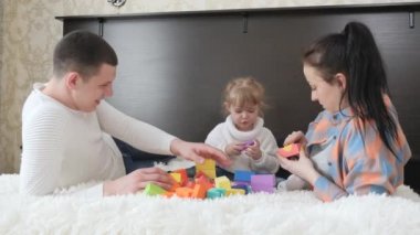 Ebeveyn, baba, anne, kız çocuk odasında, yataktaki küplerle oynuyorlar. Çocuğa oyun yoluyla öğretmek. Çocuk, baba ve anne aile evi inşa etme oyunu oynuyorlar. Mutlu bir aile. Çocuklar için eğitici oyunlar.