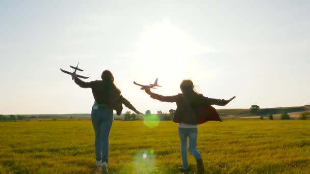Children on background of sun with an airplane in hand. Dreams of flying. Happy childhood concept. Two girls play with a toy plane at sunset. Silhouette of children playing on the plane — Stock Video