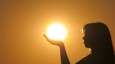 Mutlu kadın avuçlarında güneş tutuyor. Sıcak güneşin ve hayatın tadını çıkar. Gün batımında dua eden bir kız silueti. Güneş ışığı kızın ellerinde. Seyahat ve macera konsepti. Din ve Tanrı 'ya inanç.