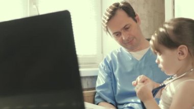 Çocuk doktoru, doktor, çocuk doktoru. Ofiste küçük bir hastayla oynuyor. Küçük bir çocuk pediyatrist tarafından muayene edilir. Doktor çocuğu steteskop ve fonendoskopla muayene ediyor. Özel klinikler.
