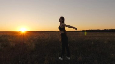 Sağlıklı, güzel bir kız şehrin dışında güneşlenir. Egzersiz ve temiz havada ısınma. Özgür genç bir kadın gün batımında yaz parkında spor yapmaya gider. Kız jimnastik yapıyor.