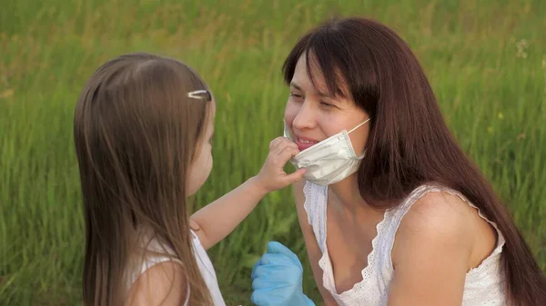 Μητέρα φορώντας μάσκα και γάντια βάζει ιατρική μάσκα στο παιδί στο πάρκο το καλοκαίρι στο δρόμο κατά τη διάρκεια της επιδημίας coronavirus. Μαμά και κόρη με ιατρικές μάσκες έξω. Ευτυχισμένη οικογένεια μαμά, κόρη αγκαλιά — Φωτογραφία Αρχείου
