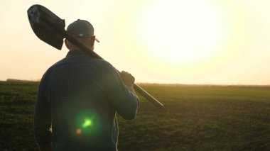 Elinde kürekle bir çiftçi elinde kürekle tarlada yürüyor. Bir tarım uzmanı gün batımında siyah verimli bir arazide yürüyor. Gün batımında tarlada küreği olan bir işçi..