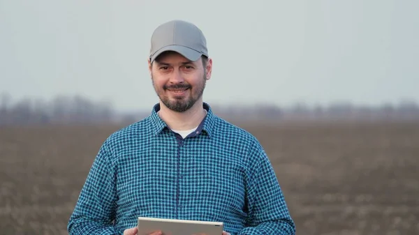 Farmer looks at tablet and camera and smiles. Business man works in field in spring with tablet. A smart agronomist with tablet in his hands checks field. Environmentally friendly agriculture — Fotografia de Stock