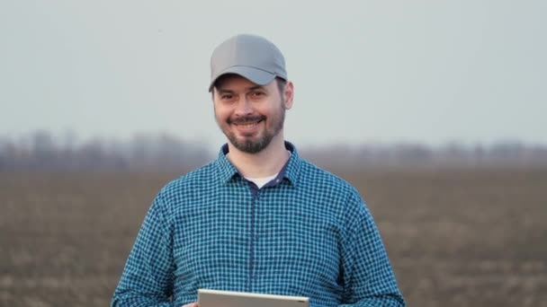 Farmer looks at tablet and camera and smiles. Business man works in field in spring with tablet. A smart agronomist with tablet in his hands checks field. Environmentally friendly agriculture — ストック動画