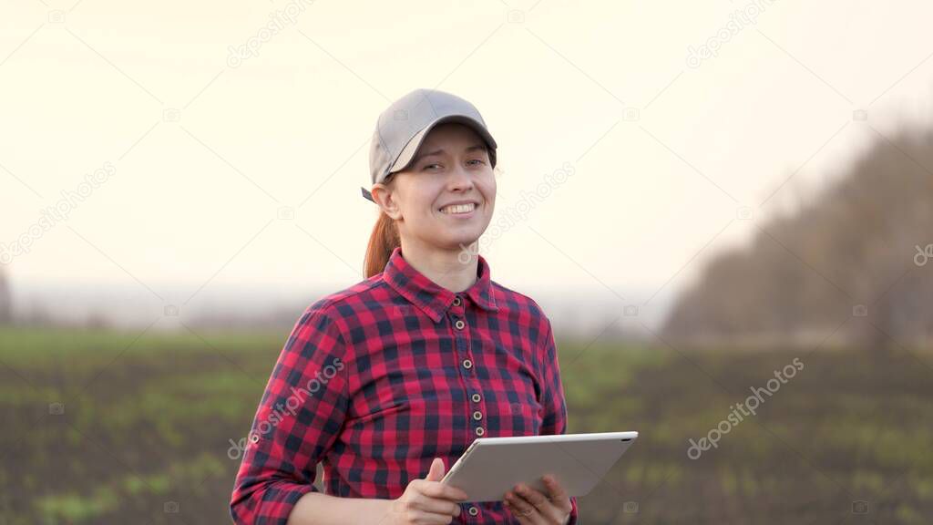 Farmer woman works with a computer tablet, smiles for camera. A smart agronomist with tablet in his hands checks field. Environmentally friendly agriculture. Modern digital technologies in agriculture