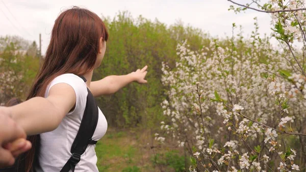 A carefree and free loving woman and man walk along a country road, and rejoice in blooming cherry trees, smiles, joy. In spring, young couple travels, holding hands, around beautiful cherry orchards. — Stockfoto