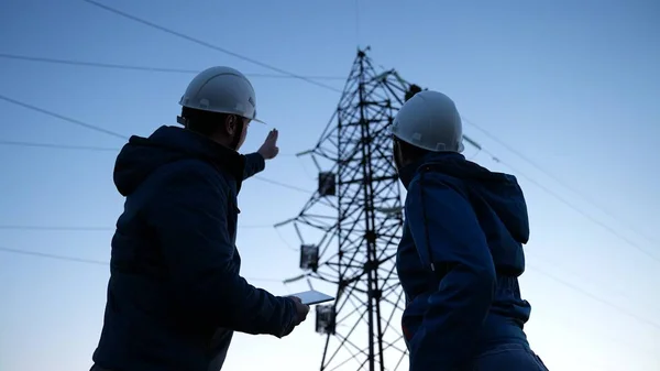 Trabalho em equipe e engenheiros, parceiros apertando as mãos, bom trabalho. Trabalhadores de energia em capacetes brancos de proteção estão verificando linha de energia on-line usando tablet computador. Conceito de negócio. Mulher e homem trabalham juntos — Fotografia de Stock