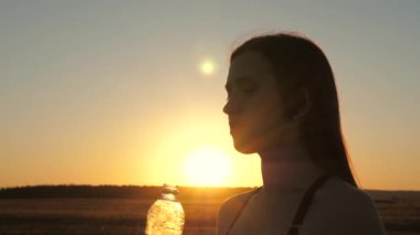 Kız baharda parkta antrenmandan sonra bir şişeden temiz maden suyu içiyor. Genç bayan dışarıda çalıştıktan sonra su içer. Yaz parkında spor.