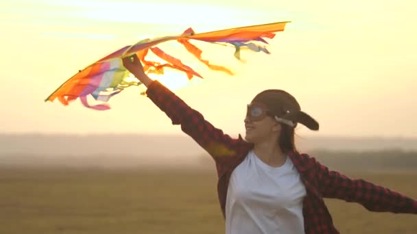 Child dreams of freedom, flight and travel. Teenager wants to become a pilot. Happy girl runs in a pilots helmet with a multi-colored kite in her hands in park. Teenager playing on a plane outdoors. — Stock Video