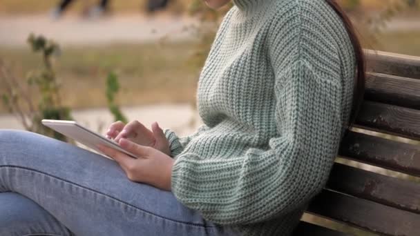 Krásná dívka student studovat na tabletu vzdáleně v parku na lavičce. Mladá žena na volné noze pracuje na dálku na moderním počítači venku. Dívka odpočívá s tabulkou v ruce.. — Stock video