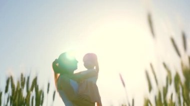 Anne ve bebek, kız yeşil buğday tarlasında yürüyor, sarılıyor ve öpüşüyorlar. Bebek annesinin kollarında. Anne ve çocuk buğday tarlasında yürüyorlar. Mutlu aile gezileri. Çiftçi kadın ve çocuk tarlada