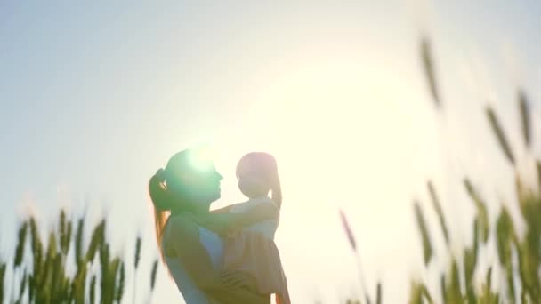 Mãe e bebê, filha estão andando no campo de trigo verde, abraçando e beijando. O bebé está nos braços das mães. Criança e mãe estão andando em um campo de trigo. Feliz viagem em família. Mulher agricultora e criança no campo — Vídeo de Stock