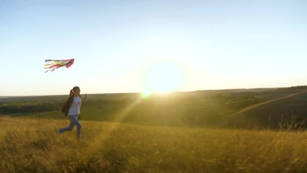 Ein glückliches Mädchen mit einem Drachen in der Hand läuft im Sonnenuntergang über das Feld. Ein unbeschwertes Kind träumt von Freiheit, Flucht. Teenager spielt im Park mit Flugzeug, will Pilot werden — Stockvideo