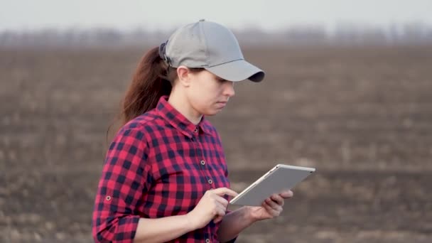 農家の女性が畑を歩き、タブレットPCで作業しています。彼の手にタブレットを持つ農学者がフィールドをチェックします。環境に優しい農業。農業における現代のデジタル技術 — ストック動画