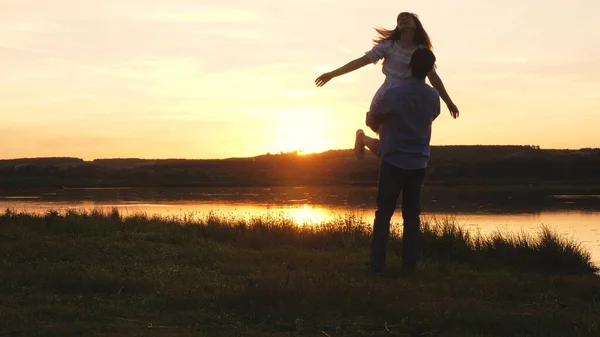 Família dançando ao pôr do sol na praia. Pessoas livres. Jovem feliz salta para os braços do seu amado homem. Um casal amoroso homem e mulher dançando em raios brilhantes de sol no fundo do lago. — Fotografia de Stock