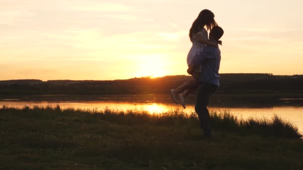 Baile familiar al atardecer en la playa. Gente libre. La joven feliz salta a los brazos de su amado hombre. Una pareja amorosa hombre y mujer bailando en brillantes rayos de sol sobre el fondo del lago. — Vídeos de Stock