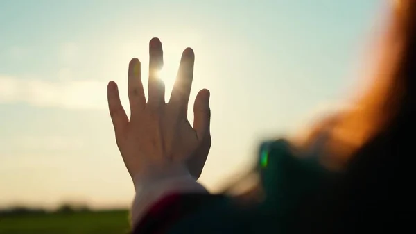 Flickan sträcker ut handen mot solen, solstrålarna skiner genom fingrarna. En lycklig flickas hand sträcker sig efter solen. Solnedgång mellan händerna på flickan. Barnens hand drömmer om att få sola. Lyckligt familjebegrepp — Stockfoto