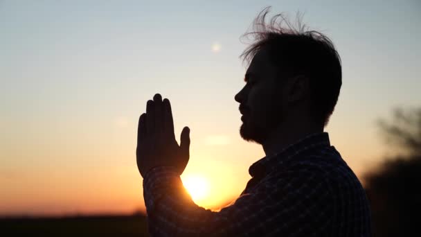 Christian man praying at sunset close-up. Men in front of the sky in the rays of the sun pray for family and children. Relaxation and meditation in nature, healthy lifestyle — Stock Video