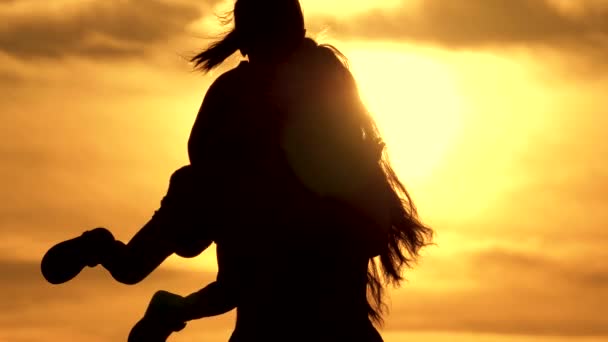 Mama umkreist ihre geliebte gesunde kleine Tochter auf dem Arm. Silhouette von Mutter und Baby bei Sonnenuntergang. glückliche Mutter und kleines Kind umarmen sich im Park auf der Natur in den Sonnenstrahlen. Familie im Urlaub. — Stockvideo