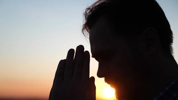 Христианин молится на закате крупным планом. Мужчины перед небом в лучах солнца молятся за семью и детей. Отдых и медитация в природе, здоровый образ жизни — стоковое фото