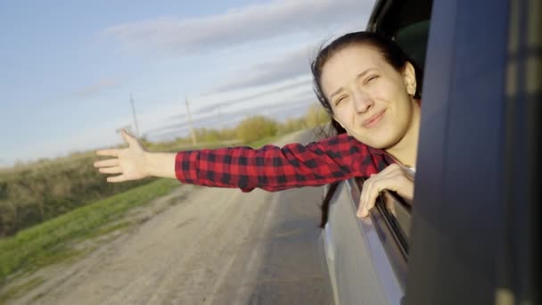 Chica libre viaja en coche coge el viento con su mano desde la ventana del coche. Mujer joven con el pelo largo se sienta en el asiento trasero del coche, se extiende a la ventana y capta el resplandor del sol. Un adolescente viaja en un coche. — Vídeos de Stock