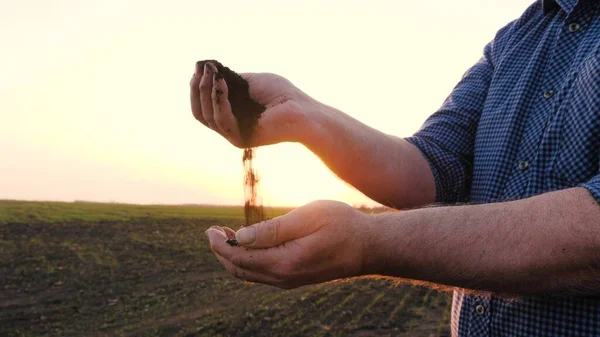 In hands of farmer, he holds handful of fertile land in sunshine on field in spring. Agriculture, agribusiness. In palms of gardener holds and pours humus, fertilized soil. Agriculture and fertility. — Stock Photo, Image