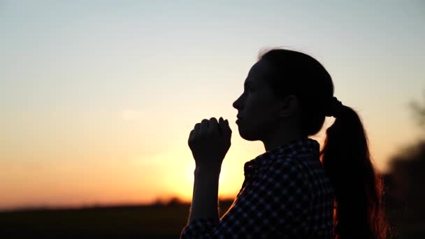 Günbatımında dua eden Hıristiyan bir kadın. Gökyüzünün arka planındaki kız güneş ışınlarında aileye ve çocuklara dua ediyor. Doğada rahatlama ve meditasyon, sağlıklı yaşam tarzı — Stok video
