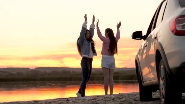 Gratis kvinder rejsende står ved siden af bil på stranden nyder solnedgang i parken, hoppe og klappe glæde. Piger chauffører stoppet på campingpladsen. Veninder nyder turen i bil. Ferie, eventyr – Stock-video