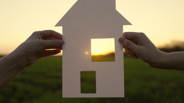 Family holds paper house at sunset, sun shines through window. Camera movement to window. Home and happiness symbol. Concept of building house for family. My dream is to build, buy house for children — Stock Video