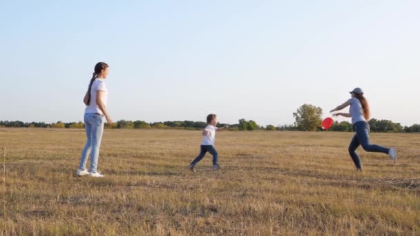 Szczęśliwa rodzina, matka i córki grają, rzucając latający czerwony dysk do siebie w parku. Piknik rodzinny z dziećmi. Dziewczyny rzucają sobie latającym spodkiem do parku. Dziecko bawi się z dorosłymi — Wideo stockowe