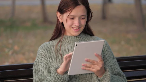 Estudante menina estudando com computador tablet ao ar livre. Freelancer trabalha online. A jovem trabalha em um tablet no parque em um banco. Uma menina usando um tablet digital imprime mensagens em uma rua da cidade. — Fotografia de Stock