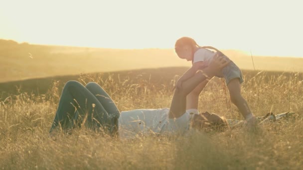 Papá juega con su hija pequeña en el parque en la hierba. Padre sostiene al bebé en sus brazos, el bebé salta volteretas, se regocija y ríe. Padre feliz y niño pequeño abrazándose en la naturaleza. Familia de vacaciones. — Vídeos de Stock