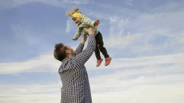 Tata wyrzuca swoją szczęśliwą córkę do błękitnego nieba w parku. Ojciec i małe dziecko bawią się, śmieją się i przytulają. Szczęśliwej rodzinnej podróży. Dziecko jest w ramionach rodzica. Weekend z tatą. Szczęśliwa rodzina. — Zdjęcie stockowe