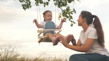 Mutlu aile annesi ve küçük kızı yaz parkında oynuyorlar. Bir anne neşeli kızını bir ağacın altında salıncakta sallıyor. Bir anne çocuğuyla oynar. Mutlu çocukluk kavramı.