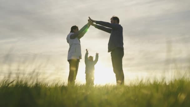 Famiglia felice che gioca con la figlioletta, simbolo di famiglia a casa al sole. Mamma è papà e raffigurano con le mani il tetto di casa sopra la testa del bambino. Sogno di una casa comune. Costruttori domestici — Video Stock