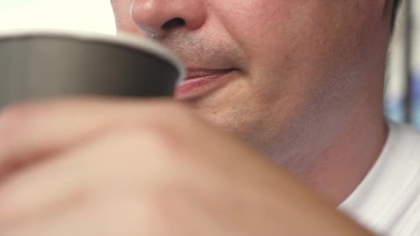 通りのカフェで熱い飲み物。サマーカフェでの快適な滞在。男は木のテーブルでお茶を飲んでいる。接近中だ。テーブルの上にコーヒーのガラスがあり、男は芳香族おいしいコーヒーを飲んでいます. — ストック動画