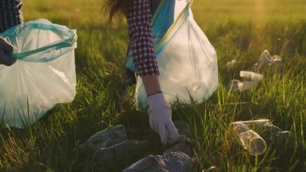 Люди займаються прибиранням пластикових сміття в парку на траві. Рука робітників піднімає пластикову пляшку з трави в алугу. Екологічно чиста планета. Людина забруднення природи — стокове відео