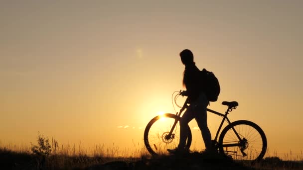 Une fille libre voyage à vélo, se repose, regarde le coucher du soleil et profite du soleil. Concept d'aventure et de voyage. Une bonne santé des jeunes promenades touristiques avec des vélos à travers le champ, profiter de la nature, l'air frais. — Video