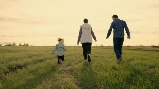 Glückliche Familie spielt und läuft im Park bei Sonnenuntergang. Teamwork in der Familie. Eltern und Tochter laufen auf grünem Gras. Fröhliches Familienwochenende im Frühling. Kinder, Eltern rennen. Glückliche gesunde Kindheit — Stockvideo