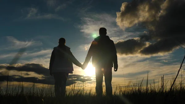 Happy people stand holding hands and watch the sunset. Teamwork. Meditation, prayer. Silhouette Couples rejoice together at sunset. A group of people hold hands towards the sun. Trust and love