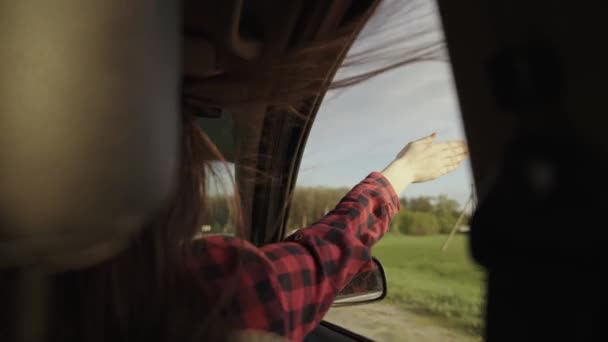 Özgür bir kadın sürücü araba kullanıyor, elini arabanın camından tutuyor. Uzun saçlı bir kız arabanın ön koltuğunda oturur, elini açık bir pencereden uzatır, yolculuğun tadını çıkarır. — Stok video