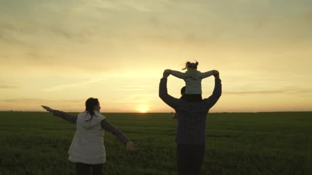 Glückliche Familie, Kind und Eltern laufen zusammen im Park bei Sonnenuntergang Silhouette. Papa, Tochter, Mama laufen wie ein Flugzeug, träumen davon, Pilot zu werden und zu fliegen. Fröhliche Familie und kleines Kind spielen auf dem Feld — Stockvideo