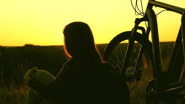 Happy woman cyclist resting in the park. Travel, adventure concept. Free girl travels with a bike at sunset. Young woman hiker sitting next to bike enjoying nature and sun, relax and meditate — Stock Photo, Image