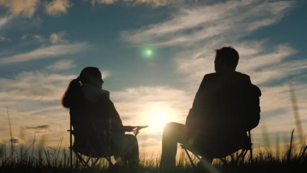 Glückliche Paare auf Date bewundern den wunderschönen Sonnenuntergang, während sie auf Reisestühlen sitzen. Liebespaar im Park hält Händchen in der Sonne. Familienreisen, Pausen auf dem Campingplatz. Glückliche Menschen in der Nähe, die Natur genießen — Stockvideo