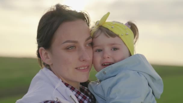 Vacker mamma och hennes dotter kramas i parken på våren, sommaren. Mamma och hennes barn leker på lekplatsen. Grabben älskar mamma. Lycklig familj mor och döttrar ler utomhus. — Stockvideo