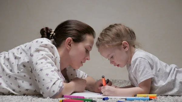 Família feliz brincando juntos em casa no chão. Criança e mãe, babá, ensina menina a desenhar. Uma mãe ajuda sua filha a aprender a desenhar em papel, colorir com lápis multicoloridos e canetas de feltro. — Fotografia de Stock