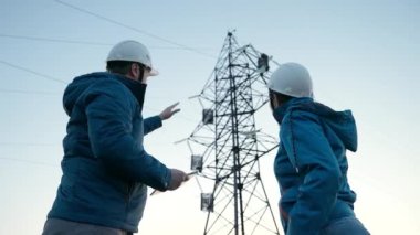 Takım çalışması ve mühendisler, ortaklar el sıkışıyor, iyi iş. İş konsepti. Kadın ve erkek birlikte çalışır. Koruyucu beyaz kasklı elektrik işçileri bilgisayar tableti kullanarak elektrik hattını kontrol ediyorlar.