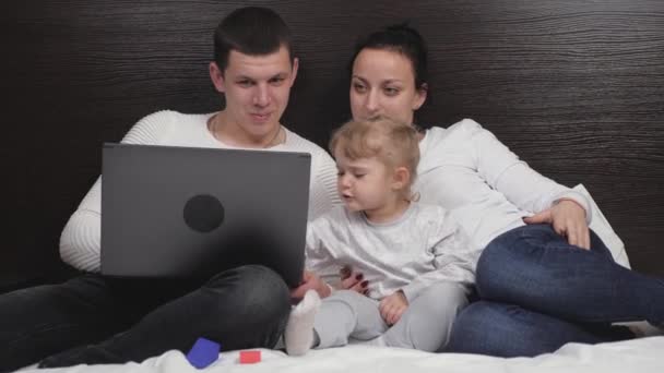Счастливая семья отдыхает вместе вечером дома с планшетом. Онлайн обучение. Маленький ребенок, дочь смотрит мультфильм онлайн с помощью цифрового планшета, весело с родительским контролем, сидя на кровати — стоковое видео